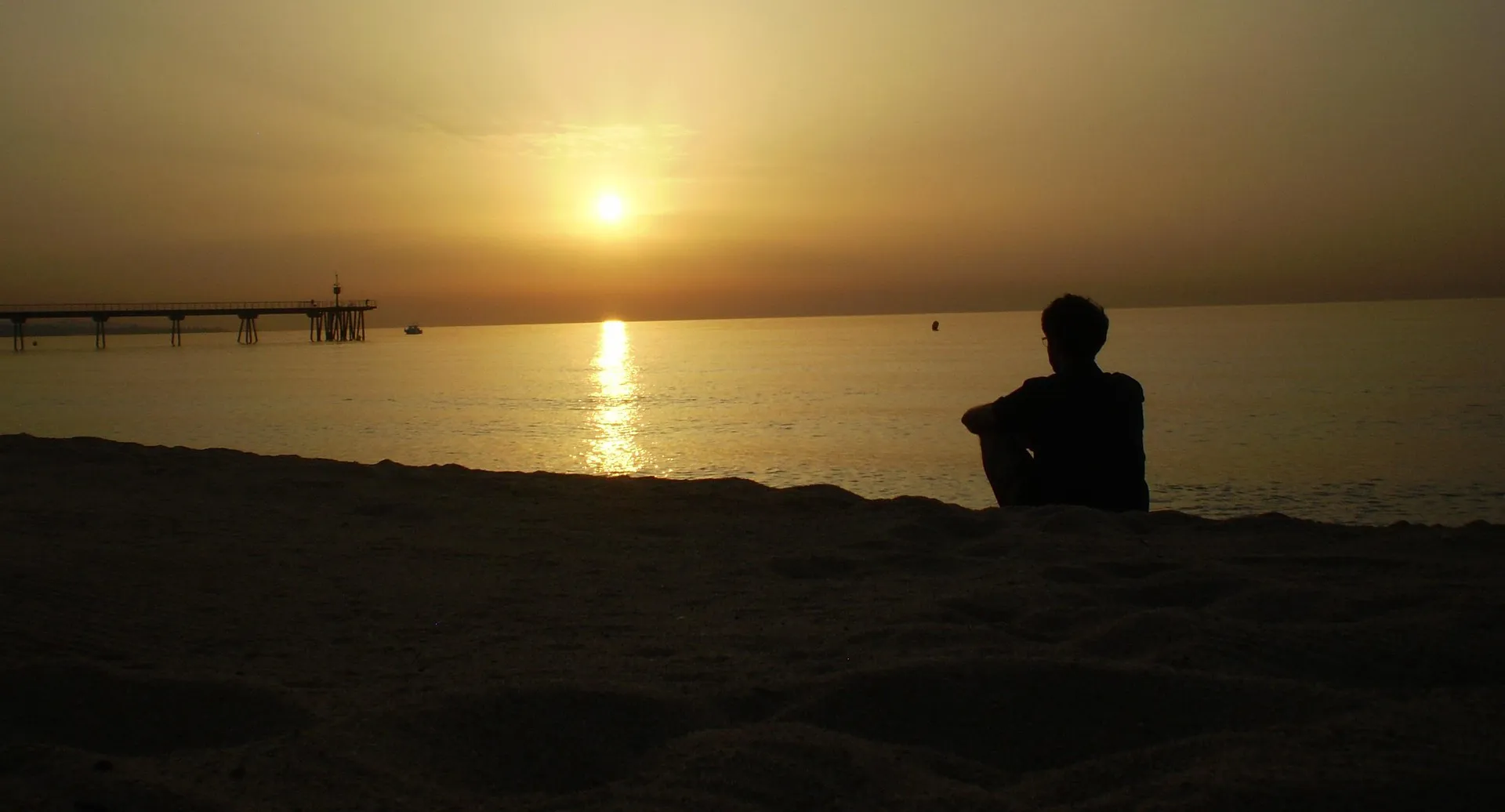 Eine Person sitzt bei Sonnenuntergang am Wasser